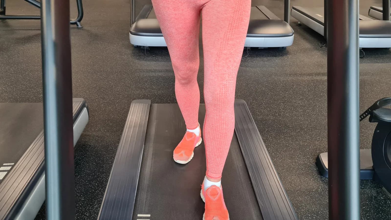 Una deportista camina con control en una cinta ligeramente inclinada sin apoyarse de forma continua en las barras