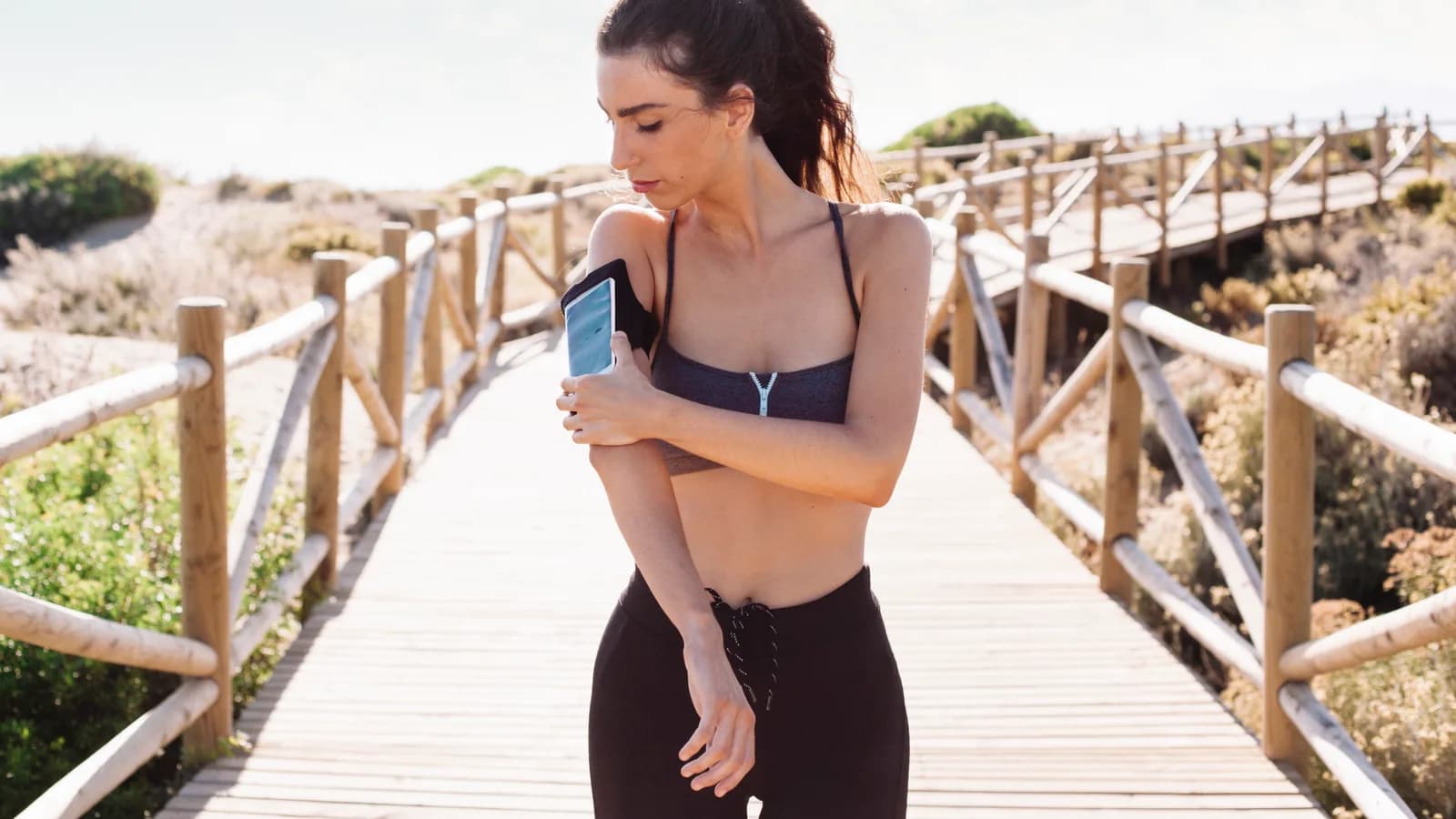 Corredor adulto guarda un teléfono sin marcas en un cinturón de running junto a un sendero